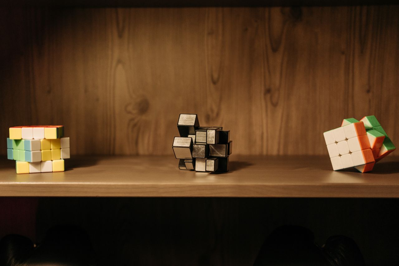 Three different puzzle cube types on a shelf: a 4x4 cube, a mirror-shape cube, and a stickerless 3x3 Rubik's Cube